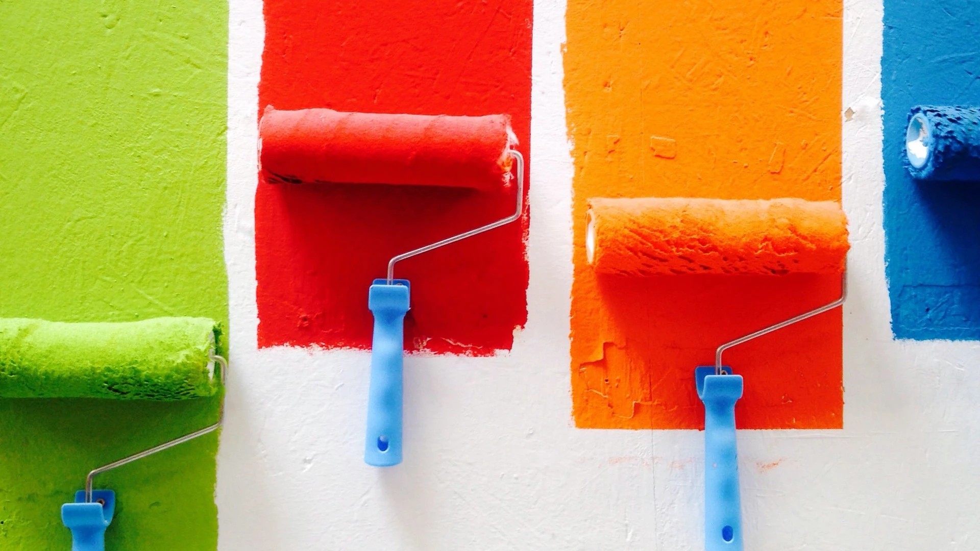 Tiras de várias cores a serem pintadas, numa parede, por rolos de pintar